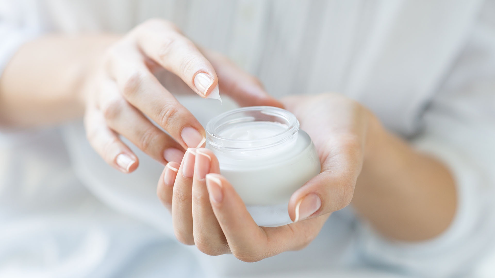 Closeup shot of hands applying moisturizer. Beauty woman holding a glass jar of skin cream. Shallow depth of field with focus on moisturizer.