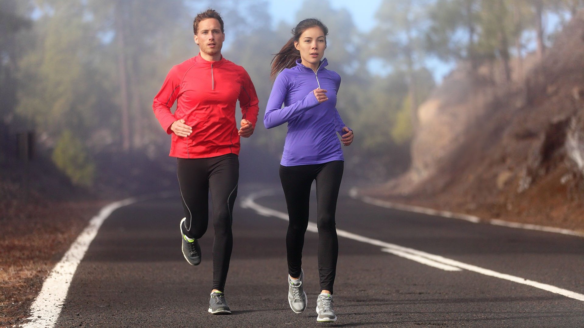 Healthy running runner man and woman workout on mountain road. Jogging male and female fitness model working out training for marathon on forest road in amazing nature landscape. Two runners execising