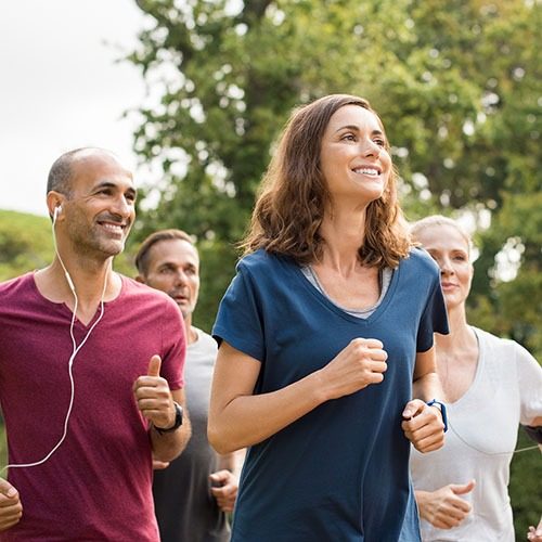 Mature woman running with group of people at park. Happy smiling woman with group of friends running together. Senior runners team on morning training.